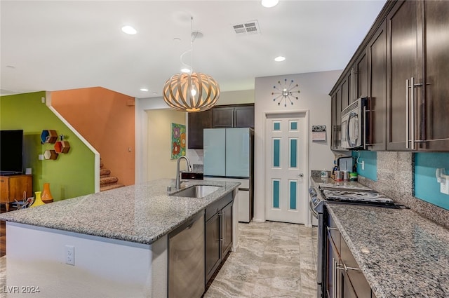 kitchen featuring sink, light stone counters, an island with sink, dark brown cabinets, and appliances with stainless steel finishes