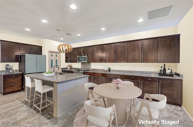 kitchen featuring sink, an island with sink, decorative light fixtures, dark brown cabinetry, and stainless steel appliances