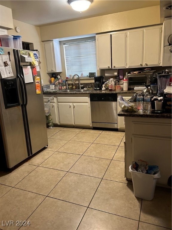 kitchen with dark stone countertops, white cabinetry, light tile patterned floors, stainless steel appliances, and sink