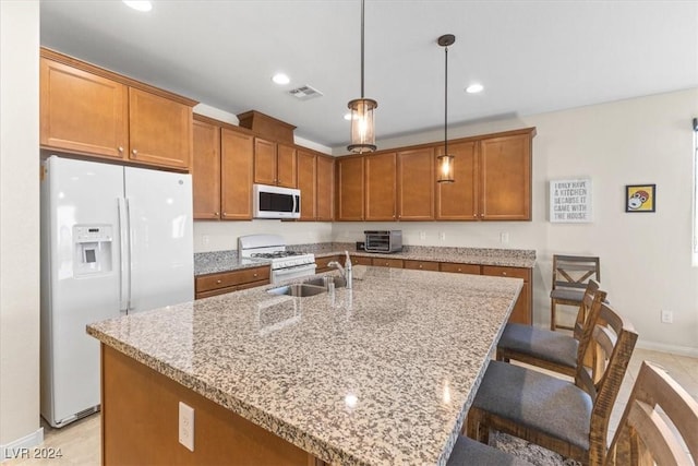 kitchen featuring decorative light fixtures, sink, a kitchen island with sink, light stone countertops, and white appliances