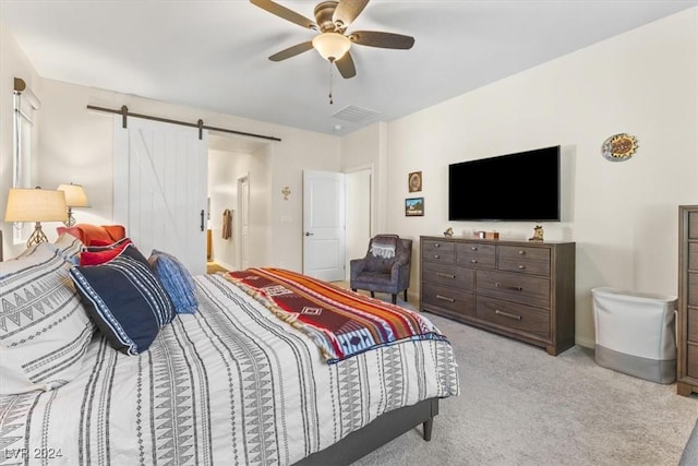 bedroom with ceiling fan, a barn door, and light carpet