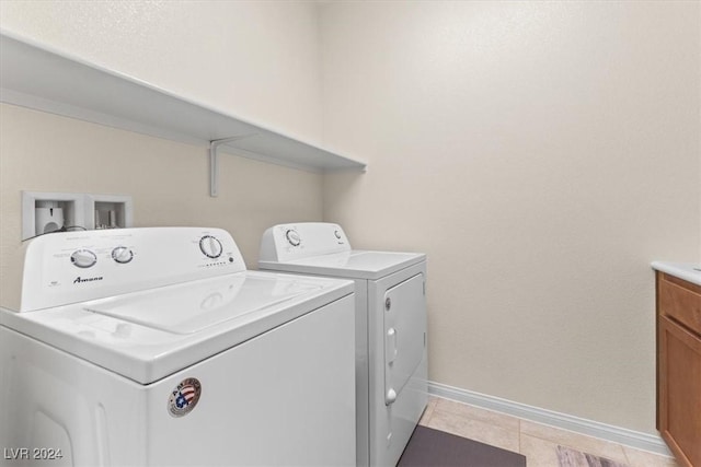 clothes washing area with light tile patterned floors, washing machine and dryer, and cabinets