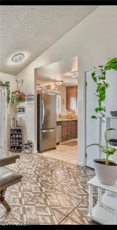 kitchen with a textured ceiling, stainless steel fridge, and vaulted ceiling