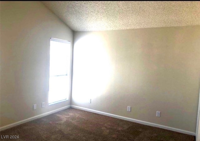 spare room with a textured ceiling, lofted ceiling, and dark colored carpet