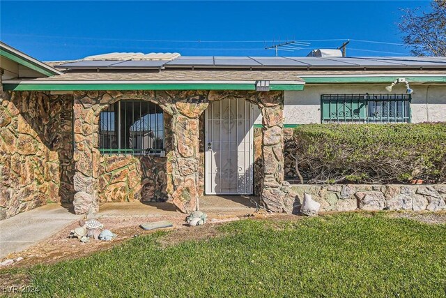 408 Rossmoyne Ave, North Las Vegas, NV 89030 - view of exterior entry with roof mounted solar panels, stone siding, and a shingled roof
