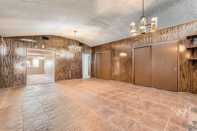 unfurnished room featuring a textured ceiling, wooden walls, and lofted ceiling