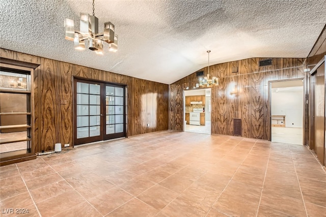 unfurnished living room with lofted ceiling, wooden walls, a chandelier, and a textured ceiling