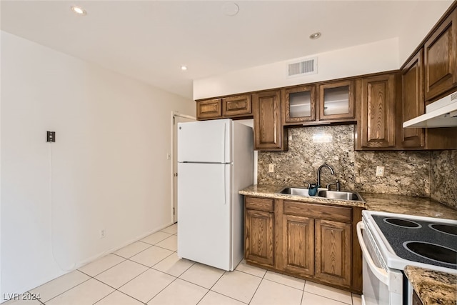 kitchen featuring white appliances, stone counters, sink, decorative backsplash, and light tile patterned floors