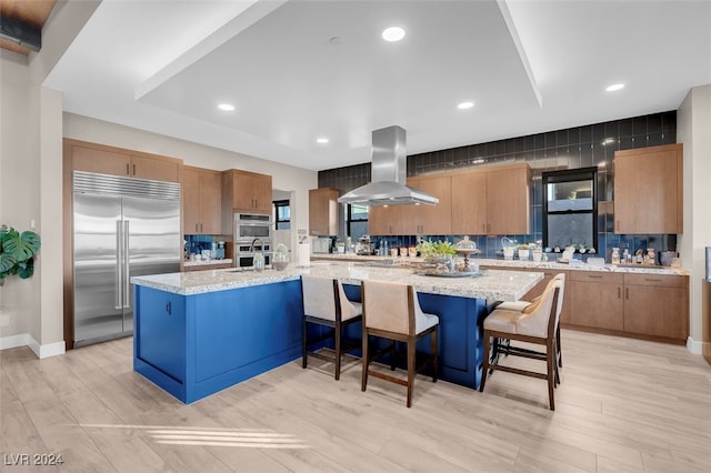 kitchen featuring a kitchen breakfast bar, range hood, a large island, light wood-type flooring, and appliances with stainless steel finishes