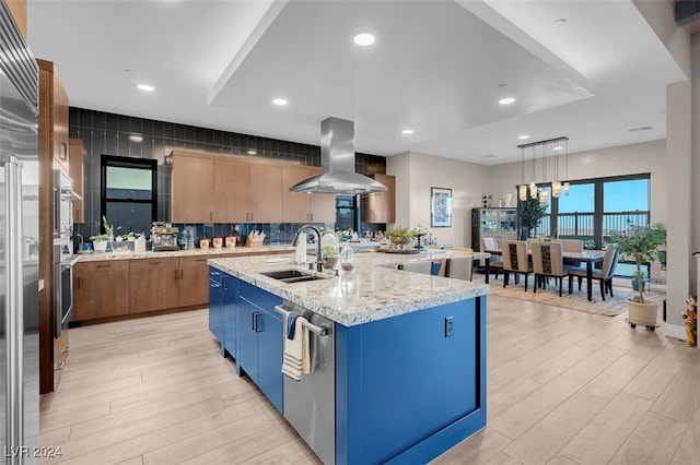 kitchen featuring sink, light wood-type flooring, island range hood, hanging light fixtures, and a center island with sink