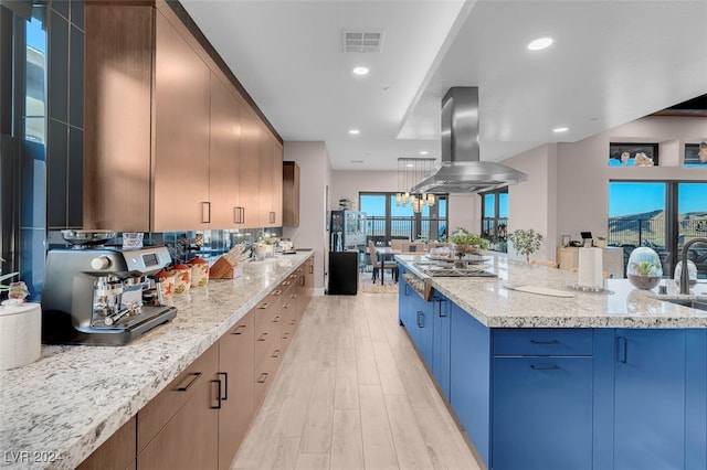 kitchen with island exhaust hood, light stone counters, light wood-type flooring, and a kitchen island