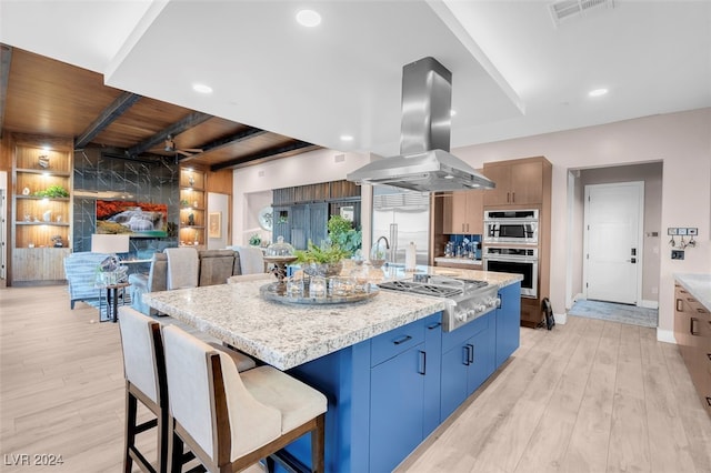 kitchen with a kitchen bar, island exhaust hood, light hardwood / wood-style floors, beamed ceiling, and a kitchen island with sink