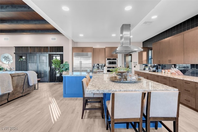 kitchen with appliances with stainless steel finishes, light hardwood / wood-style flooring, island exhaust hood, and a spacious island