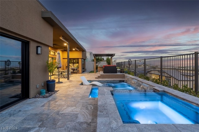 pool at dusk featuring an in ground hot tub, pool water feature, and a patio area