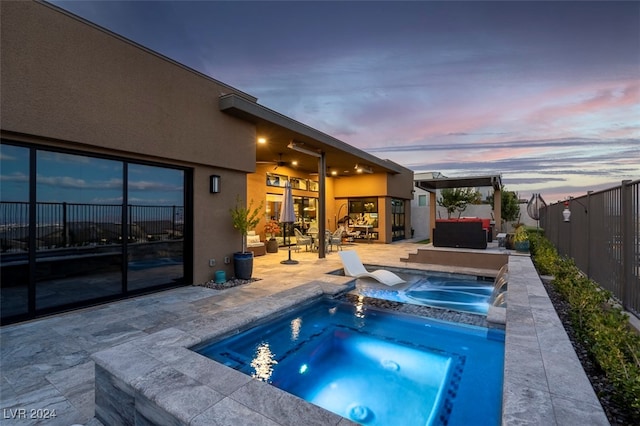 pool at dusk featuring a patio and an in ground hot tub