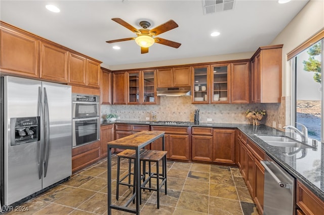 kitchen with ceiling fan, tasteful backsplash, dark stone counters, sink, and stainless steel appliances