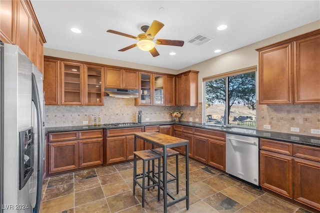 kitchen featuring ceiling fan, decorative backsplash, stainless steel appliances, dark stone countertops, and sink