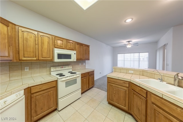 kitchen with sink, tile countertops, light tile patterned floors, and white appliances