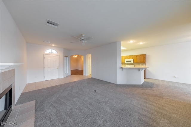 unfurnished living room featuring ceiling fan, light colored carpet, and a fireplace