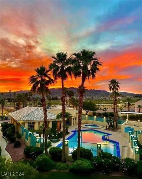 pool at dusk with a patio, a mountain view, and a hot tub