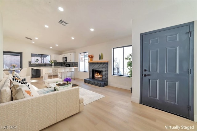 living room with a brick fireplace, vaulted ceiling, and light wood-type flooring