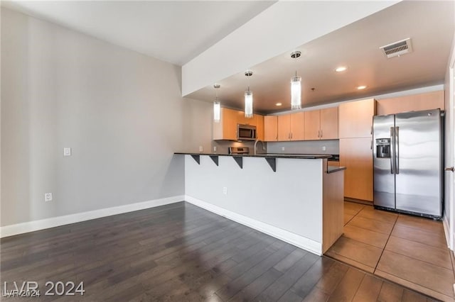 kitchen featuring appliances with stainless steel finishes, kitchen peninsula, dark hardwood / wood-style flooring, and decorative light fixtures