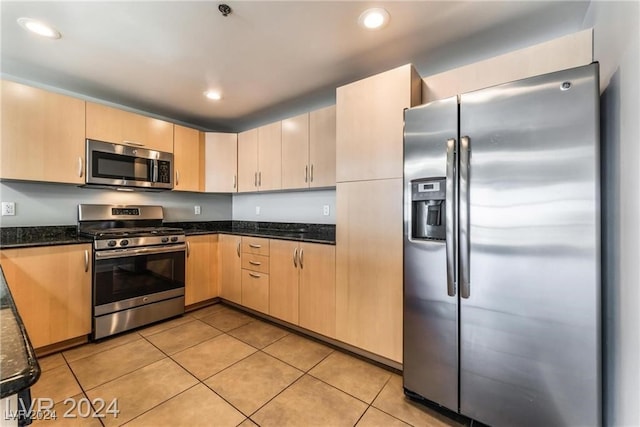 kitchen featuring dark stone countertops, light brown cabinets, appliances with stainless steel finishes, and light tile patterned floors