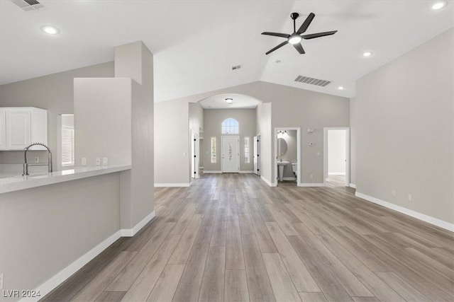 unfurnished living room featuring vaulted ceiling, sink, ceiling fan, and light wood-type flooring