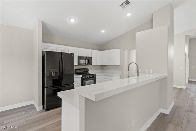 kitchen featuring black appliances, kitchen peninsula, lofted ceiling, and white cabinets