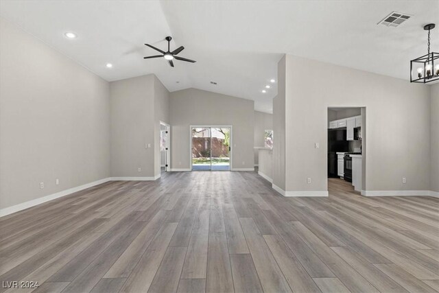 unfurnished living room featuring ceiling fan with notable chandelier, vaulted ceiling, and light hardwood / wood-style flooring