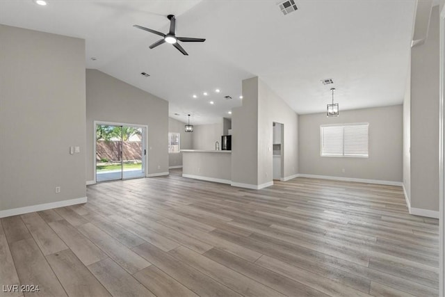 unfurnished living room with ceiling fan with notable chandelier, light hardwood / wood-style flooring, and vaulted ceiling