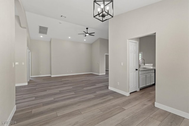 unfurnished living room with sink, light hardwood / wood-style floors, and ceiling fan with notable chandelier