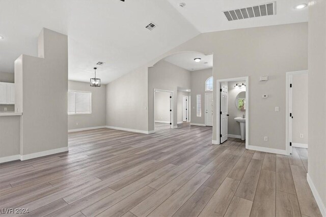 unfurnished living room with an inviting chandelier, light hardwood / wood-style flooring, and high vaulted ceiling