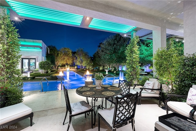 pool at night featuring pool water feature and a patio