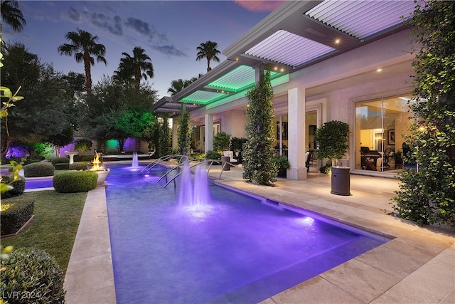 pool at dusk with pool water feature and a patio area