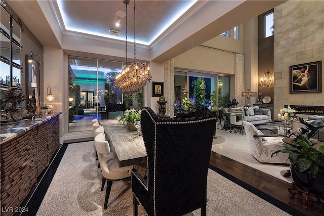 carpeted dining space featuring a high ceiling, a tiled fireplace, a tray ceiling, and a notable chandelier