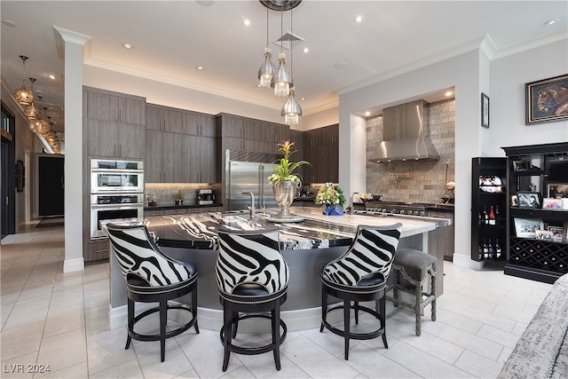 kitchen featuring appliances with stainless steel finishes, tasteful backsplash, wall chimney exhaust hood, dark brown cabinets, and decorative light fixtures