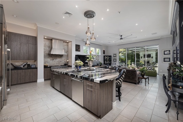 kitchen with a center island, wall chimney exhaust hood, decorative backsplash, a breakfast bar, and light tile patterned flooring