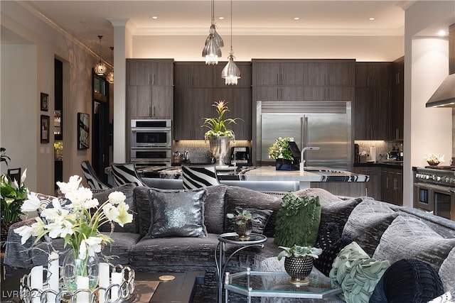 kitchen featuring backsplash, premium appliances, dark brown cabinetry, crown molding, and hanging light fixtures