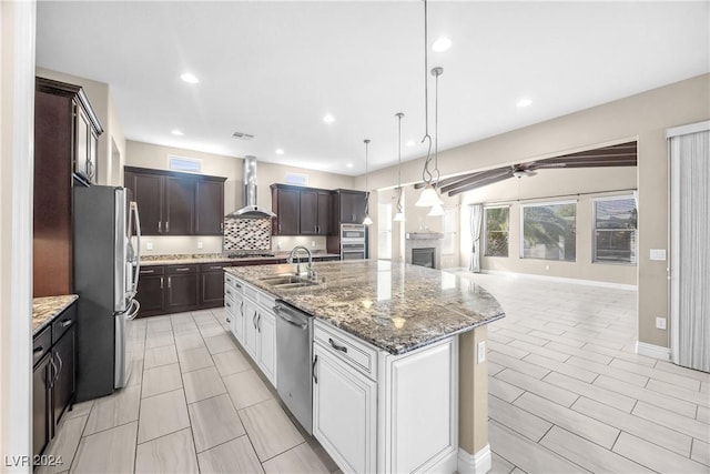 kitchen featuring a kitchen island with sink, white cabinets, wall chimney range hood, sink, and appliances with stainless steel finishes