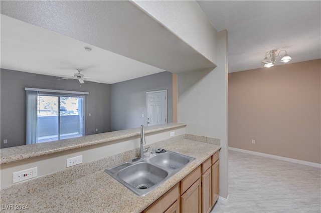 kitchen with light stone counters, ceiling fan, and sink