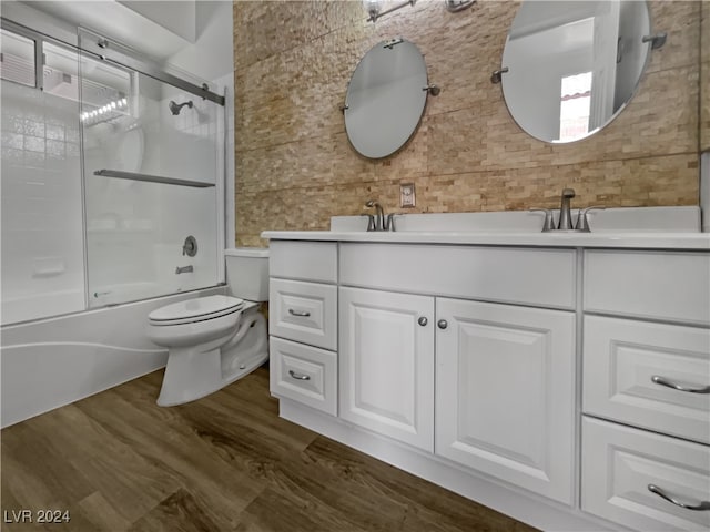 full bathroom featuring vanity, bath / shower combo with glass door, hardwood / wood-style flooring, toilet, and decorative backsplash