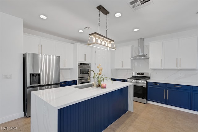 kitchen featuring a kitchen island with sink, hanging light fixtures, wall chimney exhaust hood, stainless steel appliances, and blue cabinetry