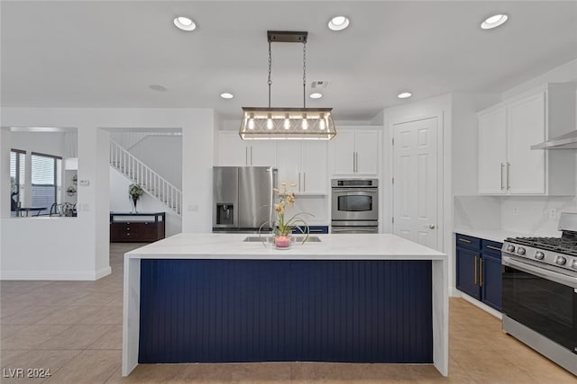 kitchen with appliances with stainless steel finishes, white cabinetry, an island with sink, blue cabinetry, and decorative light fixtures