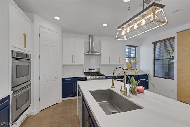 kitchen with appliances with stainless steel finishes, blue cabinets, wall chimney exhaust hood, pendant lighting, and sink