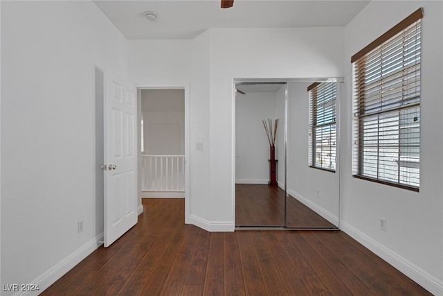 unfurnished bedroom with multiple windows, dark wood-type flooring, and a closet