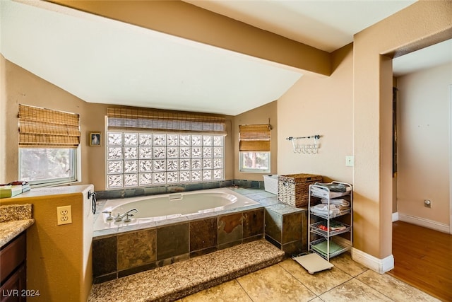 bathroom featuring lofted ceiling, tiled tub, tile patterned flooring, and vanity