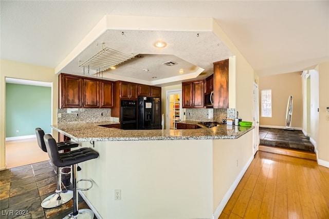 kitchen with black appliances, wood-type flooring, a breakfast bar, tasteful backsplash, and kitchen peninsula