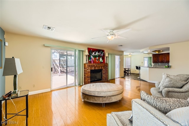 living room featuring ceiling fan, light wood-type flooring, and a brick fireplace