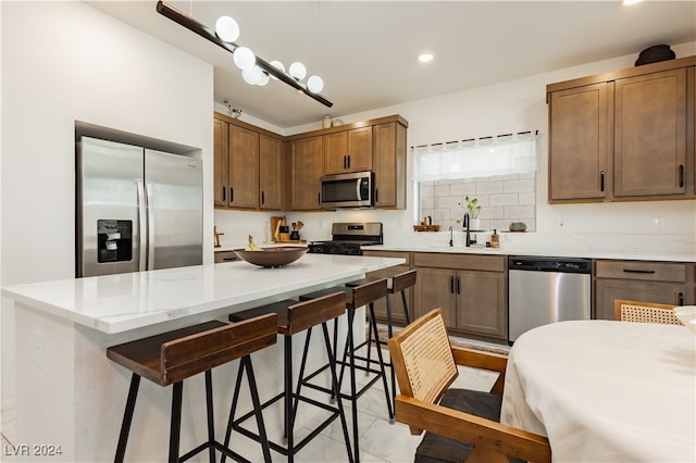 kitchen with appliances with stainless steel finishes, decorative backsplash, a breakfast bar, light tile patterned floors, and sink